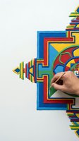 Artist hand carefully placing colored sand to create a vibrant geometric mandala with red, blue, yellow, and green patterns.