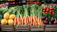 Fresh organic produce displayed in wooden crates at farmers market including vibrant carrots, lemons, beets and leafy greens arranged in rustic style for healthy eating.