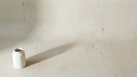 Minimalist white ceramic vase casting long shadow on textured concrete surface in natural light creating modern architectural interior design composition.