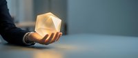Close-up of a hand holding a glowing geometric crystal or gem stone with warm light, representing innovation, energy, and business success for corporate design.