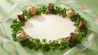 Overhead view of golden candles arranged in circle with fresh green parsley wreath on striped pastel fabric, creating festive table centerpiece for holiday entertaining and seasonal decoration.