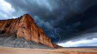 Lightning strike illuminates dramatic red rock formation against dark stormy sky, capturing raw power of nature in desert landscape during thunderstorm.