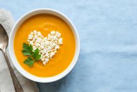 Creamy orange soup with heart-shaped cottage cheese garnish and fresh parsley in white bowl on blue wooden background for healthy cooking concepts.