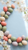 Pastel speckled Easter eggs arranged in a frame border on soft blue linen with spring cherry blossoms, copy space for text.