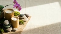 Zen spa composition with bamboo candles, smooth stones, green moss, and pink orchid on linen background for wellness and relaxation.