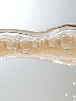 Macro shot of champagne or sparkling wine bubbles forming along liquid surface, showing transparent spheres and golden hues in crystal clear detail.