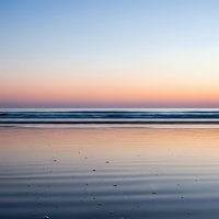 Serene ocean waves reflecting pastel sunset colors on wet sand beach creating peaceful coastal atmosphere for relaxation and meditation backgrounds.