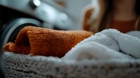 Fresh clean towels in wicker basket, orange and white cotton terry cloth with soft focus background, for spa and wellness marketing content.