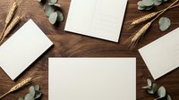 Blank white papers arranged on wooden surface with dried wheat stalks and eucalyptus leaves for stationery design, branding, and flat lay composition projects.