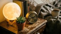 Cozy bedside table with glowing moon lamp, vintage alarm clock, succulent plant, coffee cup and books creating warm atmospheric home decor scene.
