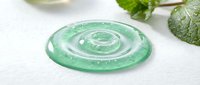 Green cosmetic gel serum drop with bubbles on white surface near fresh mint leaves, skincare product texture closeup for beauty and wellness.