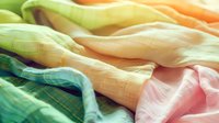 Colorful silk fabric waves in soft pastel shades of green, orange and pink creating gentle flowing curves and folds with delicate texture and light effects.
