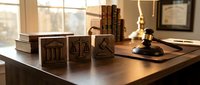 Wooden blocks with legal symbols including scales of justice, courthouse, and gavel on lawyer desk in warm office setting for legal education concepts.