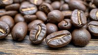 Fresh roasted coffee beans with visible groove lines scattered on rustic wooden surface, macro shot showing rich brown color and natural texture for cafe marketing.