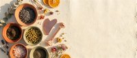 Flat lay arrangement of various seeds and spices in terracotta bowls with dried citrus slices and flowers on neutral beige background for culinary and wellness content.