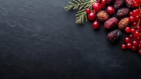 Fresh red currants and dried dates with green pine branch on black slate stone background with copy space for seasonal holiday design.