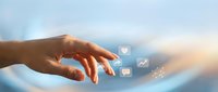 Hand reaching toward floating digital icons representing communication and technology in soft blue sky background with warm sunlight.