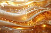 Golden liquid waves with bubbles and light reflections create dynamic flowing pattern. Macro photography captures honey or oil abstract movement.