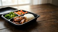Healthy meal prep container with grilled chicken, white rice, steamed broccoli and carrots on wooden table. Ready-to-eat balanced lunch box for fitness diet.