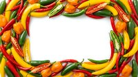 Colorful hot chili peppers arranged in a frame border on white background, featuring red, yellow, and green varieties for food and cooking content.