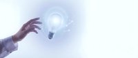 Hand reaching toward glowing light bulb with digital particles and bright ethereal background representing innovation, creativity and breakthrough ideas.