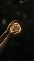 Female hands gently holding glowing golden orb of light against dark background with bokeh effects for spiritual and energy healing concepts.