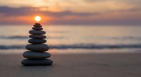 Balanced stone stack on beach at sunset with warm golden light reflecting on calm ocean waves creating peaceful meditation and zen atmosphere.