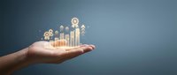 Caucasian hand holding glowing bar charts, gears, and growth icons against blue background, representing business growth, financial planning, and strategic development for corporate presentations.