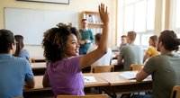 African American female student raising hand enthusiastically in classroom setting with diverse classmates during interactive learning session.