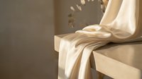 Soft ivory silk fabric draped elegantly over a stone surface in warm natural light, evoking luxury, minimalism, and refined home decor aesthetics.
