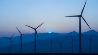 Wind turbines generating renewable energy at twilight with mountain silhouettes and purple sky creating sustainable power landscape for environmental projects.