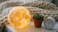 Glowing moon lamp creates cozy atmosphere on bedside table with succulent plant and alarm clock. Perfect for bedroom decor and relaxation ambiance.