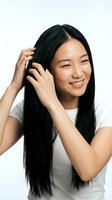 Young East Asian woman with long black hair, wearing white t-shirt, touching hair with hand and smiling at camera. Suitable for beauty, haircare, wellness and lifestyle marketing.