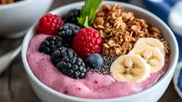 Healthy breakfast bowl with pink smoothie, fresh berries, sliced banana, granola and chia seeds served in white ceramic bowl. Close up food photography.