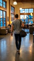 Young man walking through modern coffee shop interior with gym bag during evening hours with warm ambient lighting and large windows.