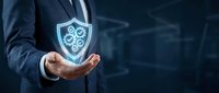Businessman in dark suit holding glowing shield icon with gear symbol, representing cybersecurity, data protection, and network security solutions for enterprise business.