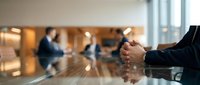 Professional businessman with clasped hands at conference table during corporate meeting with colleagues in modern office boardroom for business strategy.