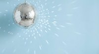 Silver disco ball reflecting light rays against pale blue background creating sparkle effect for party celebration and nightclub entertainment.