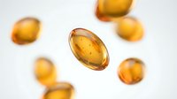 Golden amber vitamin E capsules floating on white background for health and wellness supplement marketing materials.