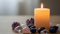 Burning candle with healing crystals and gemstones on wooden surface creating peaceful meditation and wellness atmosphere for relaxation.