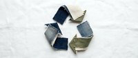 Recycled denim fabric scraps arranged in circular arrow pattern on white background, symbolizing sustainable fashion and circular economy textile reuse.