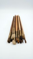 Collection of wooden artist brushes with natural bristles and brass ferrules arranged in a row on white background for painting and creative projects.