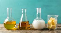 Laboratory glassware with colorful liquids and substances on wooden table against turquoise background for scientific research and chemistry experiments.