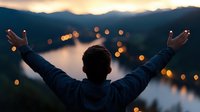 Man with raised arms enjoying sunset view over mountain lake with glowing city lights below, expressing freedom and achievement in nature.
