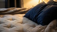 Cozy bedroom scene with navy blue pillows resting on a quilted beige mattress, warm lighting creating a relaxing atmosphere. Suitable for home decor, bedding, and interior design projects.