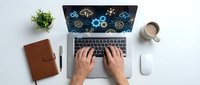 Professional working on laptop with digital technology icons, hands typing on keyboard with coffee and notebook on white desk workspace.