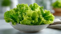 Fresh green lettuce leaves in ceramic bowl on kitchen counter for healthy salad preparation and cooking.