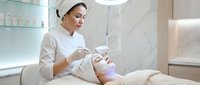 Professional cosmetologist performing facial treatment on female client in modern spa salon with advanced skincare equipment and sterile environment.