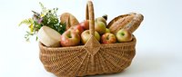 Wicker basket filled with fresh produce including apples, bread, vegetables and herbs on white background for grocery, farmers market and food delivery concepts.
