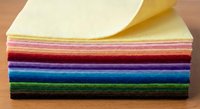 Colorful felt fabric sheets stack in rainbow colors for crafting and sewing projects on wooden surface.
